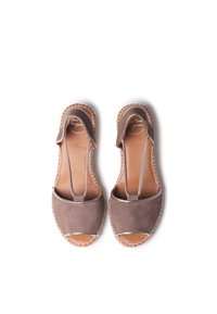 Sandalias de ante marrón con puntera abierta, correas elásticas y detalles trenzados alrededor de la suela. Diseño plano con una plantilla de cuero natural.