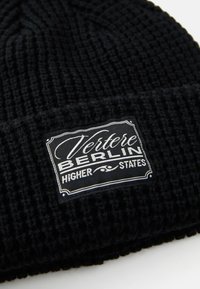 Black knitted beanie with a textured pattern, featuring a rectangular label that reads "Vertere Berlin Higher States" in white.