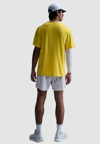 Camiseta amarilla de manga corta, pantalones cortos blancos y una gorra blanca. Presenta un diseño ligero, textura suave y un soporte para los brazos.