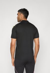 Black short-sleeve polo shirt with a classic collar, featuring a smooth texture and a subtle yellow accent on the shoulder. Simple design.