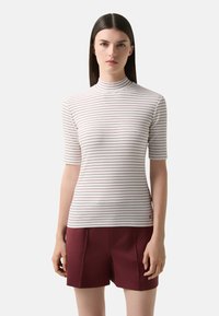 Hvid ribbet t-shirt med tynde maroon striber, høj halsudskæring og korteærmer, parret med burgunder shorts med frontfold.