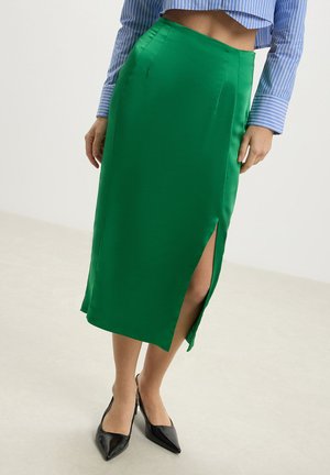 Jupe midi en satin vert avec une fente sur le côté, dotée d'une taille ajustée et d'une texture lisse. Associée à un haut court rayé bleu et blanc.