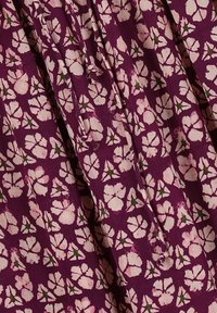 Tissu violet avec un motif floral de fleurs roses entourées de feuilles vertes ; texture douce et design légèrement plissé.