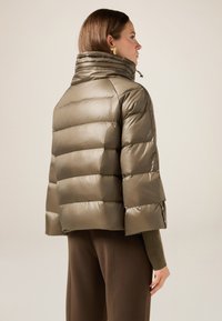 Chaqueta puffer de color verde oliva con cuello alto, que presenta segmentos acolchados horizontales y una textura brillante. Equipado con un cordón ajustable.