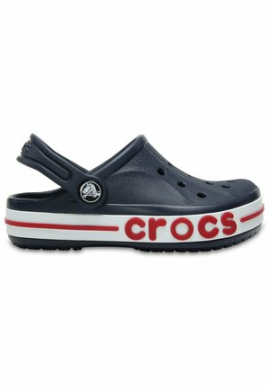 Zueco Crocs azul marino con orificios de ventilación, correa ajustable en el talón y suela blanca con texto "crocs" en rojo y detalle de raya.