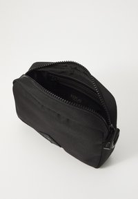 Black nylon pouch with a zip closure, rectangular shape, textured surface, and a small logo tag on the side. Interior with multiple compartments.
