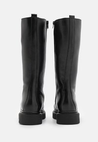 Černé kožené vysoké boty až ke kolenům s hladkou texturou, zaoblenou špičkou a bočním zipem. Masivní gumová podrážka a viditelné švy.
