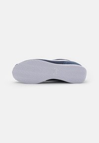Semelle d'une chaussure Nike bleu marine avec un motif de bande de roulement en zigzag blanc et le logo Nike au centre sur un fond blanc uni.