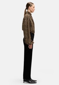 Blusa de cuello con estampado de leopardo en marrón y negro, combinada con pantalones negros de cintura alta. El calzado consiste en botines negros de tacón puntiagudo.