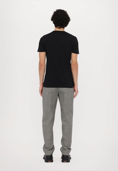 T-shirt noire à manches courtes associée à un pantalon à carreaux gris et à des baskets noires. L'ensemble présente un design minimaliste et une coupe décontractée.