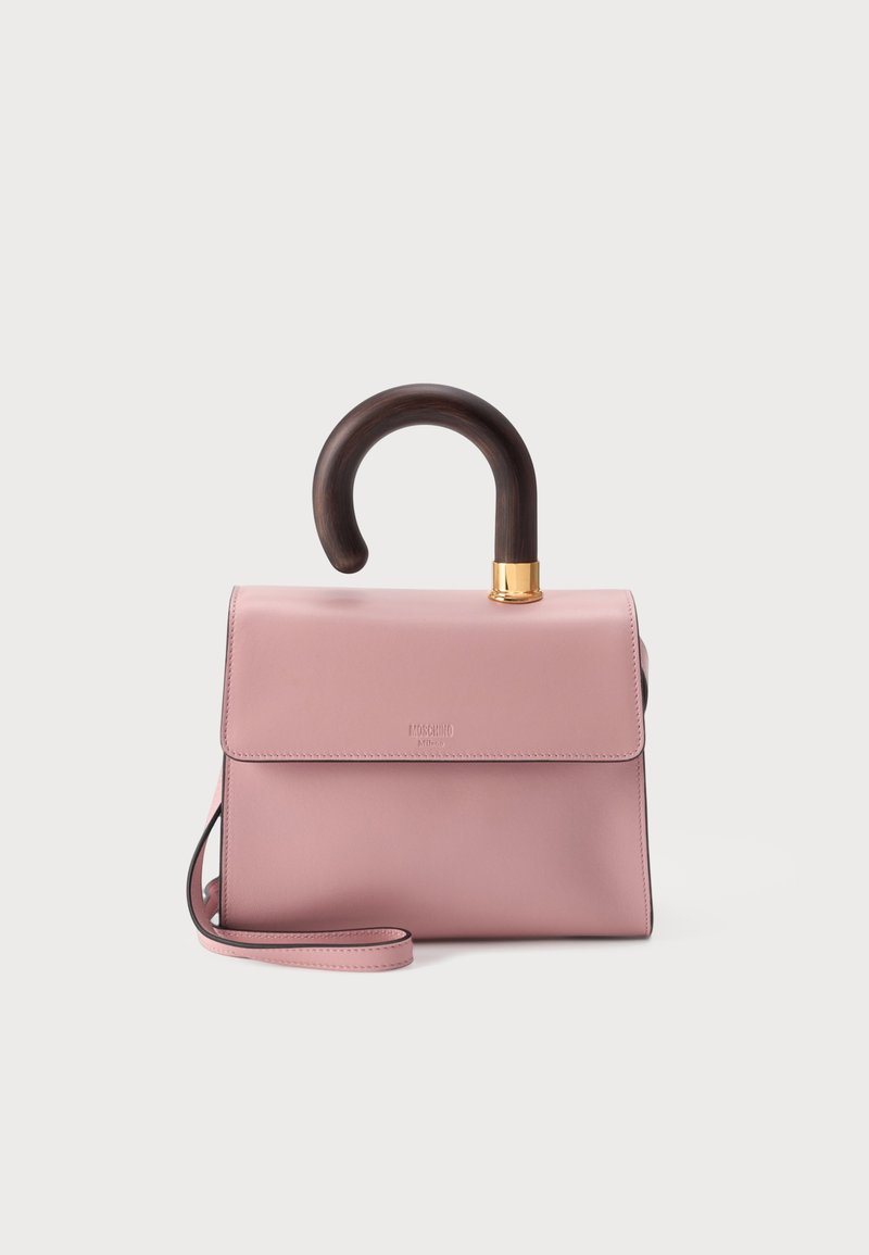 Sac à main rose clair avec une poignée en bois courbée foncée et une bandoulière rose assortie, placé sur un fond clair uni.