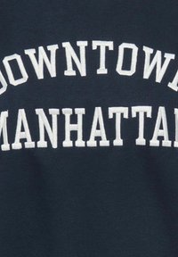 Tissu bleu marine avec un texte brodé blanc disant « DOWNTOWN MANHATTAN » en lettres grasses de style universitaire.