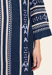 Rochie de marină, cu modele complexe de broderie albă și albastră, țesătură texturată și mâneci trei sferturi, care evidențiază un design detaliat.