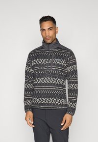 Pull-over en polaire à motifs gris avec un col zippé demi, des designs géométriques blancs et une poche poitrine avec un logo. Tissu texturé.
