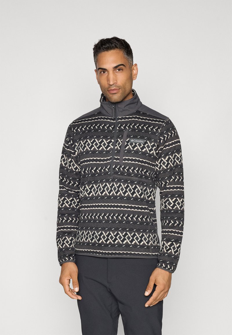 Pull-over en polaire à motifs gris avec un col zippé demi, des designs géométriques blancs et une poche poitrine avec un logo. Tissu texturé.