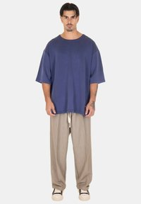 T-shirt azzurra in cotone oversize con maniche corte, abbinata a pantaloni grigi chiari a pieghe larghi e sneakers bianche con dettagli neri.