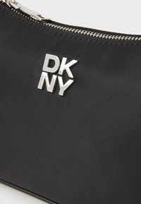 Fekete nylon tasak ezüst cipzárral és "DK NY" logóval. Érdemes felület, letisztult dizájnnal, különféle kiegészítők számára megfelelő.