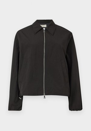 Sort jakke med lange ærmer, sølvfarvet lynlås foran, spids krave og to sidelommer på en lysegrå baggrund.