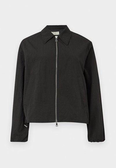 Μαύρο μακρυμάνικο μπουφάν με ασημένιο φερμουάρ στο μπροστινό μέρος, μυτερό γιακά και δύο πλαϊνές τσέπες σε ανοιχτό γκρι φόντο.