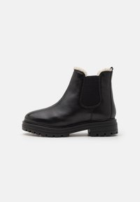 Bottines en cuir noir avec un panneau latéral élastique texturé, une doublure en fausse fourrure et une semelle robuste pour une bonne traction. Design classique Chelsea.