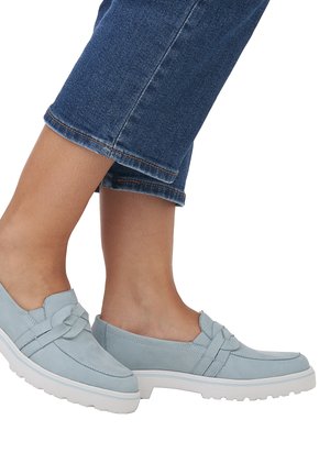 Helle blaue Wildleder-Slipper mit diagonaler Riemenverzierung, weißen Sohlen und runder Zehenform. Getragen mit dunkelblauen, knöchellangen, cropped Jeans.