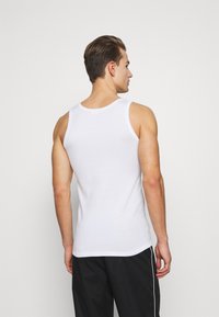 Hvid bomulds tanktop med rund halsudskæring og tætsiddende pasform, med smalle stropper og en glat tekstur. Sorte sportshorts synlige.