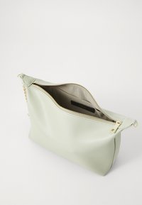 Borsa a pochette di pelle verde chiaro con una cerniera dorata e dettagli a catena. L'interno è foderato con un tessuto beige e presenta un'etichetta del produttore.