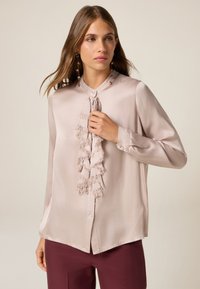 Langärmlige, hellbeige Bluse mit einem gerafften Vorderteil, Knöpfen entlang der Knopfleiste und einer glatten, samtigen Textur.