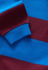 Texturovaná pletenina s vodorovnými pruhy v jasně modré a tmavě bordó, doplněná modrým žebrovaným lemem.