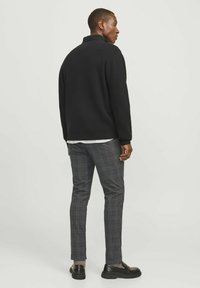 Schwarzer Strickpullover mit hohem Kragen, kombiniert mit grauen Karo-Hosen. Das Outfit hat eine lockere Passform und minimale Details.