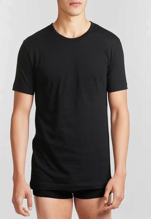 T-shirt nera in cotone con maniche corte, scollatura tonda, texture liscia, design aderente, indossata con pantaloni corti neri. Semplice e di colore uniforme.