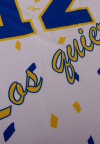 Witte stof met blauw en geel gestileerde tekst en kleurrijke confetti-achtige vormen verspreid over het oppervlak. Glad textuur.