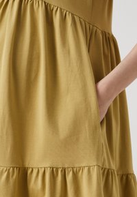 Mustár sárga ruha, tiered ruffle dizájnnal és oldalsó zsebbel. Puha, sima anyag, laza fazon és ráncolt varrás a deréknál.