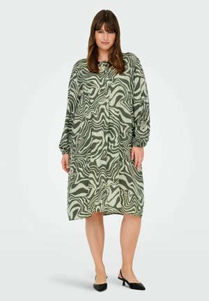Groene en witte jurk met een patroon, lange mouwen, losse pasvorm en een ronde halslijn. Gepaard met zwarte slingback schoenen.