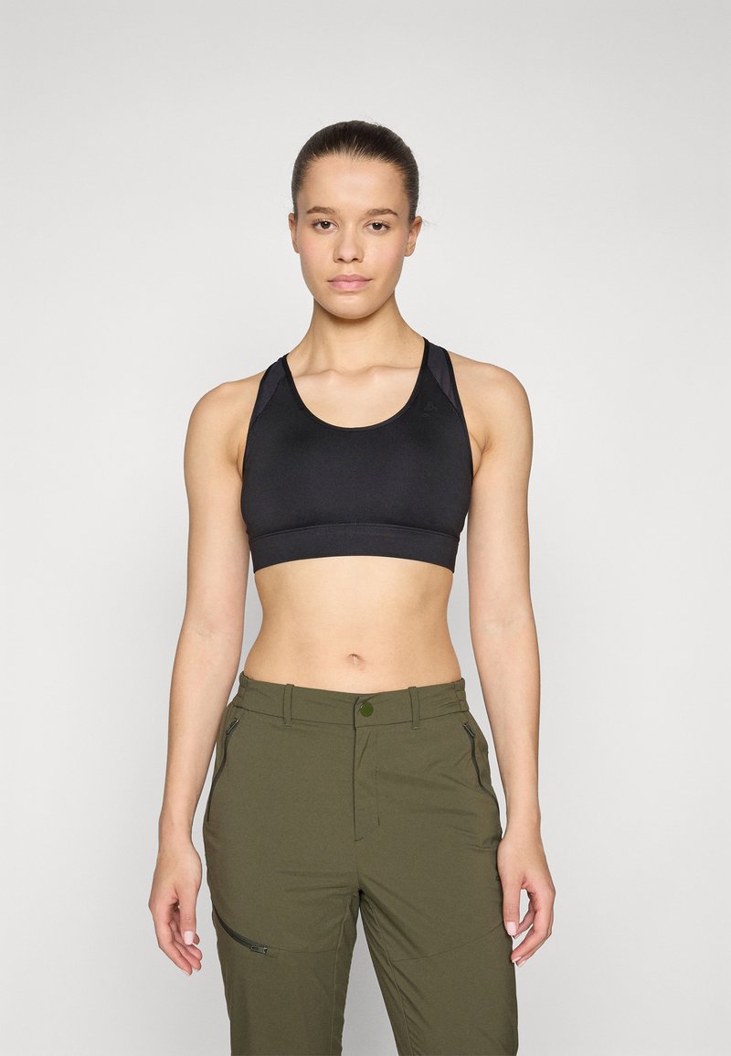 Sujetador deportivo negro fabricado con un tejido suave, con tirantes anchos y un diseño corto. Combinado con pantalones outdoor verde oliva con cremalleras.