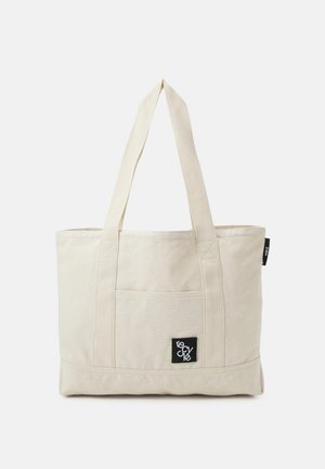 Beige lærredstaske med to skulderremme, forlomme og en sort label med teksten "recycle" i hvid skrift.