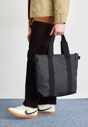 Fekete vászontáska tartós anyagból, dupla fogantyúkkal, egyszerű téglalap alakú designnal és sima textúrával. Nincsenek látható minták vagy díszítések.