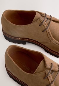 Brune ruskindssko med snøredesign, tekstureret overdel, kontrastsyninger og slidstærk gummisål med tekstureret greb.