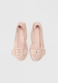 Sapatilhas de camurça rosa com bico arredondado e destaque de fivela quadrada proeminente. Textura suave e detalhes costurados ao longo das bordas.