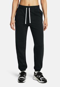 Zwarte joggingbroek van zacht materiaal met een elastische tailleband, witte koorden en taps toelopende boorden. Heeft een logo op de linkerheup.