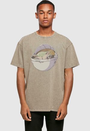 Beige cotton t-shirt with a round neck and dropped shoulders. Features a graphic of a character in a pod, printed on the front.