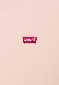 T-shirt rosa chiaro con un'etichetta ricamata rossa del logo Levi's sul lato sinistro. Il tessuto è liscio e presenta un design classico a collo rotondo.