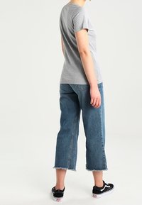 Grå kortärmad t-shirt kombinerad med ljusblå korta jeans med fransade fållar. Skorna är svarta sneakers med vita detaljer.