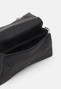 Czarna skórzana torba na ramię o teksturowanej powierzchni, srebrnych okuciach i dwóch przegrodach. Zapięcie na zatrzask oraz wytłaczane logo marki.