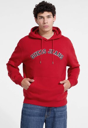 Haut à capuche rouge avec une poche frontale, un cordon de serrage à la capuche et le logo "GUESS JEANS" brodé en blanc et noir sur la poitrine. Matière en coton.