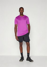 Tricou sport mov cu mâneci scurte și decolteu rotund, asortat cu pantaloni scurți negri. Adidași negri cu accente albe. Textură netedă.