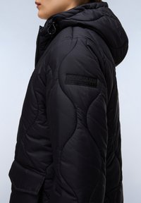 Svart isolerad jacka med en texturerad, vadderad design. Har huva, framdragkedja och en logotyp på ärmen. Hållbart material.