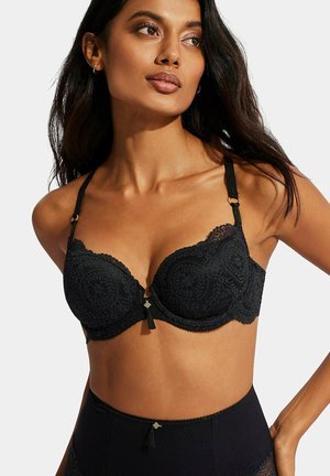 Soutien-gorge noir avec des détails en dentelle, bonnets rembourrés et un accent de nœud central. Les bretelles sont réglables avec des accessoires décoratifs et des bords festonnés.