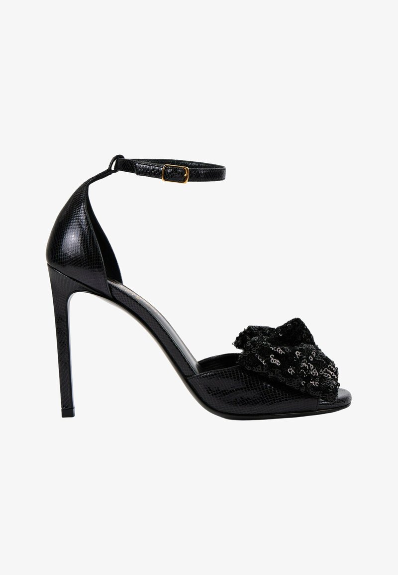 Sandale noire à talon haut avec bride cheville, matériau texturé et un nœud décoratif à sequins sur l’orteil ouvert.