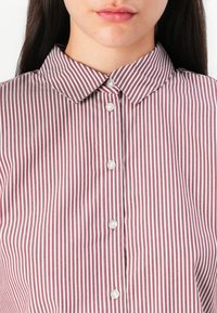 Button-up shirt with a maroon and white vertical striped pattern, featuring a pointed collar and white buttons along the front.